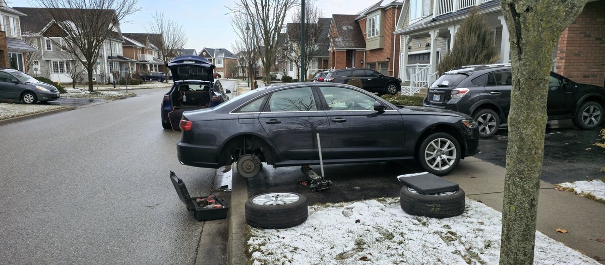 Dark Audi sedan on a jack at the curb during a Sparky X mobile tire service in Ajax — rear wheel off