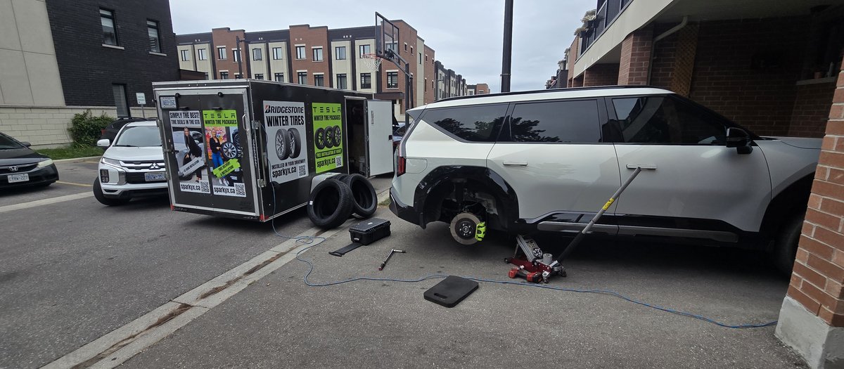 White Kia EV9 SUV on a jack during a Sparky X mobile tire service in Oshawa — the Sparky X trailer with branding behind