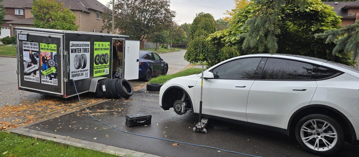 White Tesla SUV on a jack during a Sparky X mobile tire service in Scarborough — the service trailer with stacked tires behind