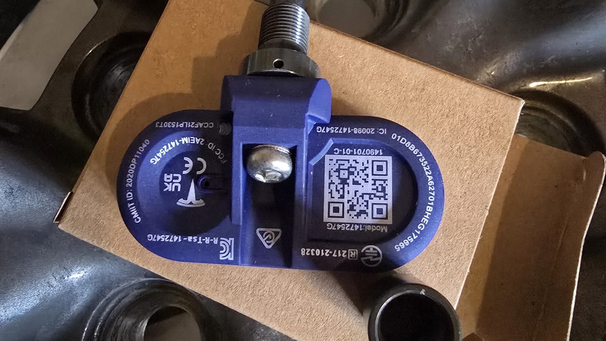 TPMS service by Sparky X — a blue Tesla Bluetooth TPMS sensor on its cardboard box resting on a wheel, valve stem and sensor markings visible