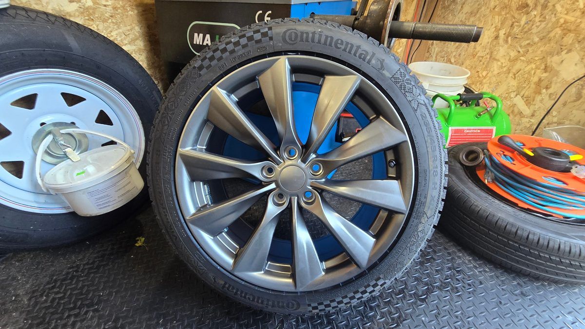 Wheel balancing by Sparky X — a Continental VikingContact 8 winter tire (235/45R18) mounted on a gunmetal turbine wheel, standing by the balancer inside the mobile trailer, the trailer's spare wheel at the left